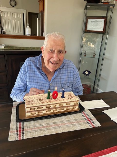 An elderly man is sitting at a table with a birthday cake and candles.