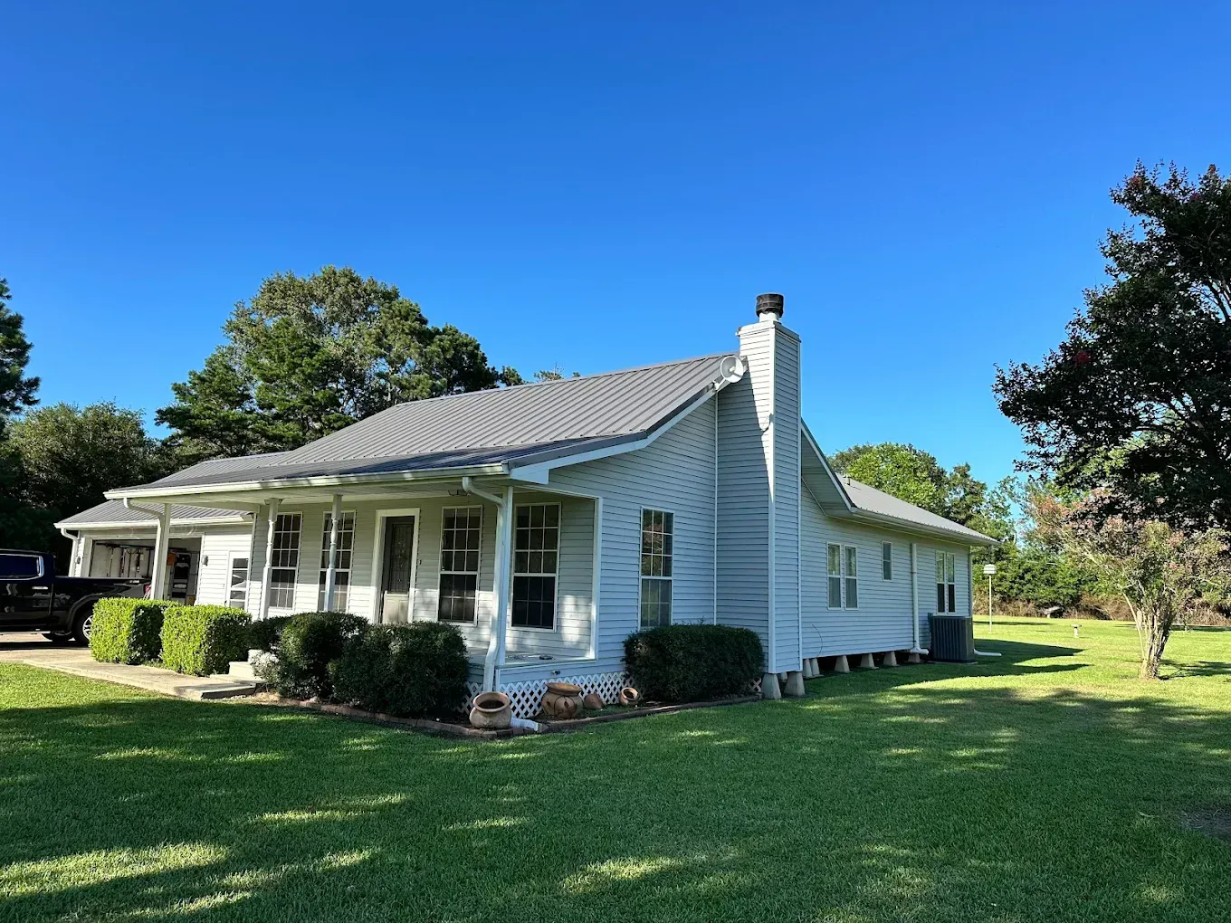 White house with porch, chimney, and green lawn under a blue sky.