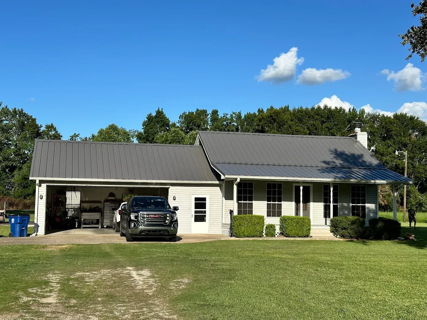 House with gray roof and carport. Police vehicle parked in carport. Green lawn, blue sky.