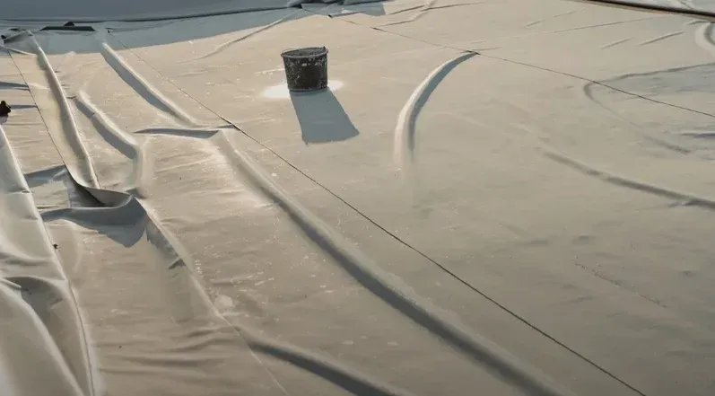A light-colored flat roof with ripples and a cylindrical vent, with a long shadow.