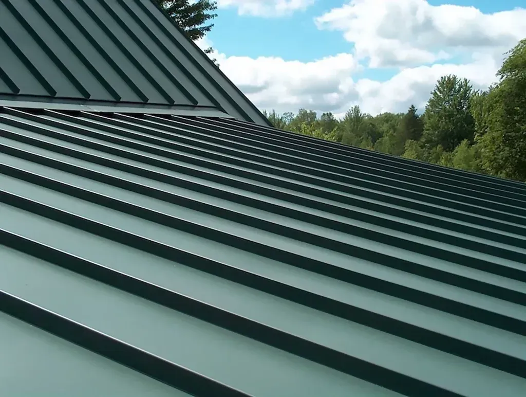 Green metal roof with vertical ribbing against a blue sky and trees.