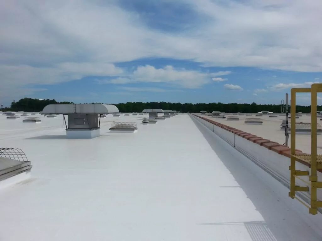White commercial roof with vents, safety rails, and a yellow ladder under a blue sky.