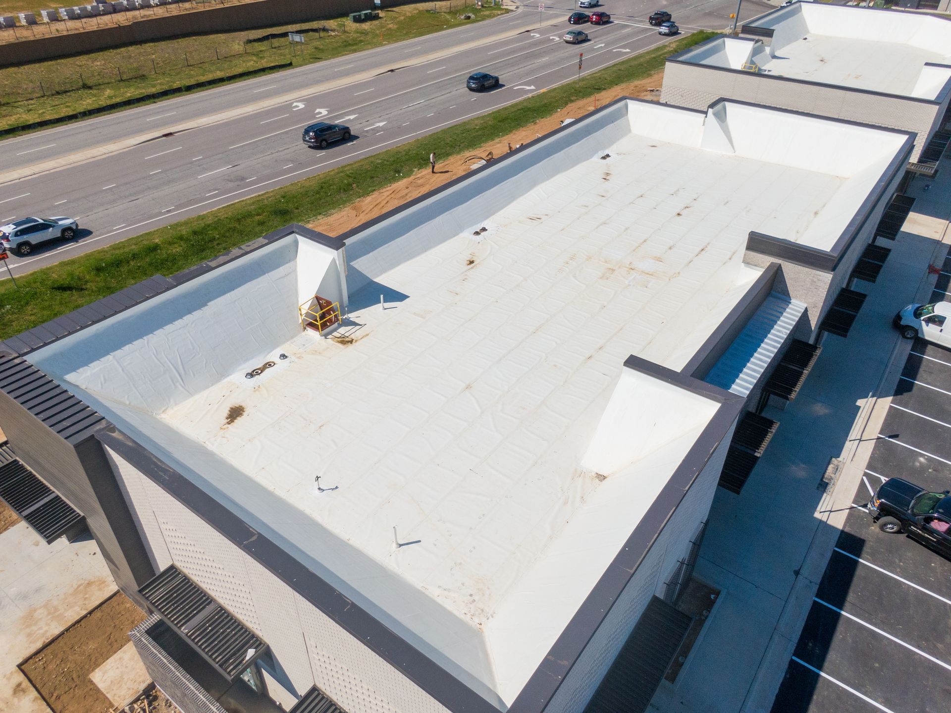 Aerial view of a white flat commercial roof next to a highway and parking lot.