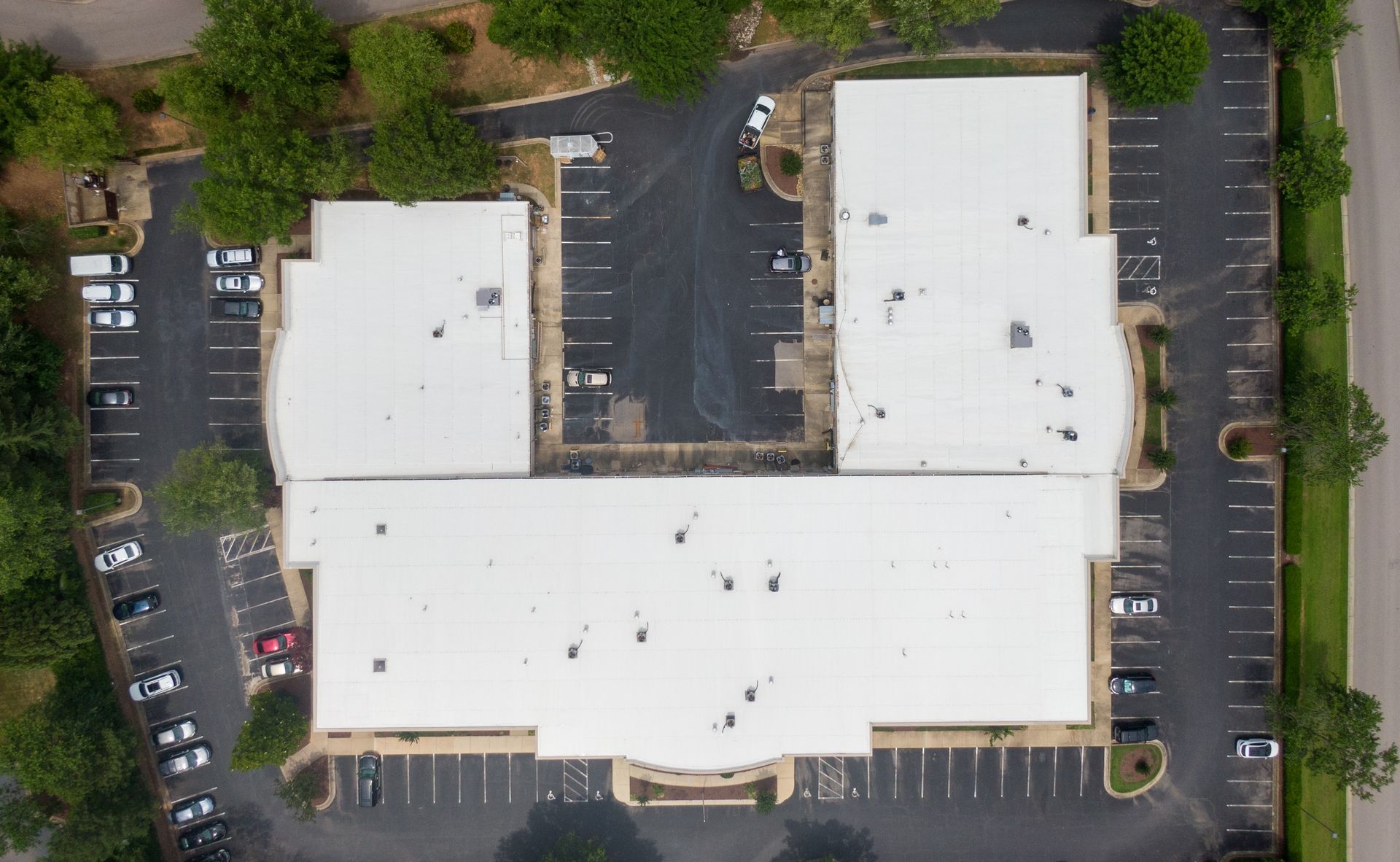 Aerial view of a white-roofed commercial building with surrounding parking areas and trees.