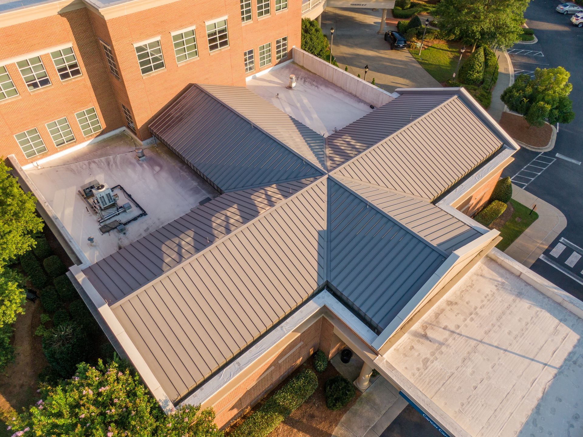 Aerial view of a brick building with a gray metal cross-shaped roof.