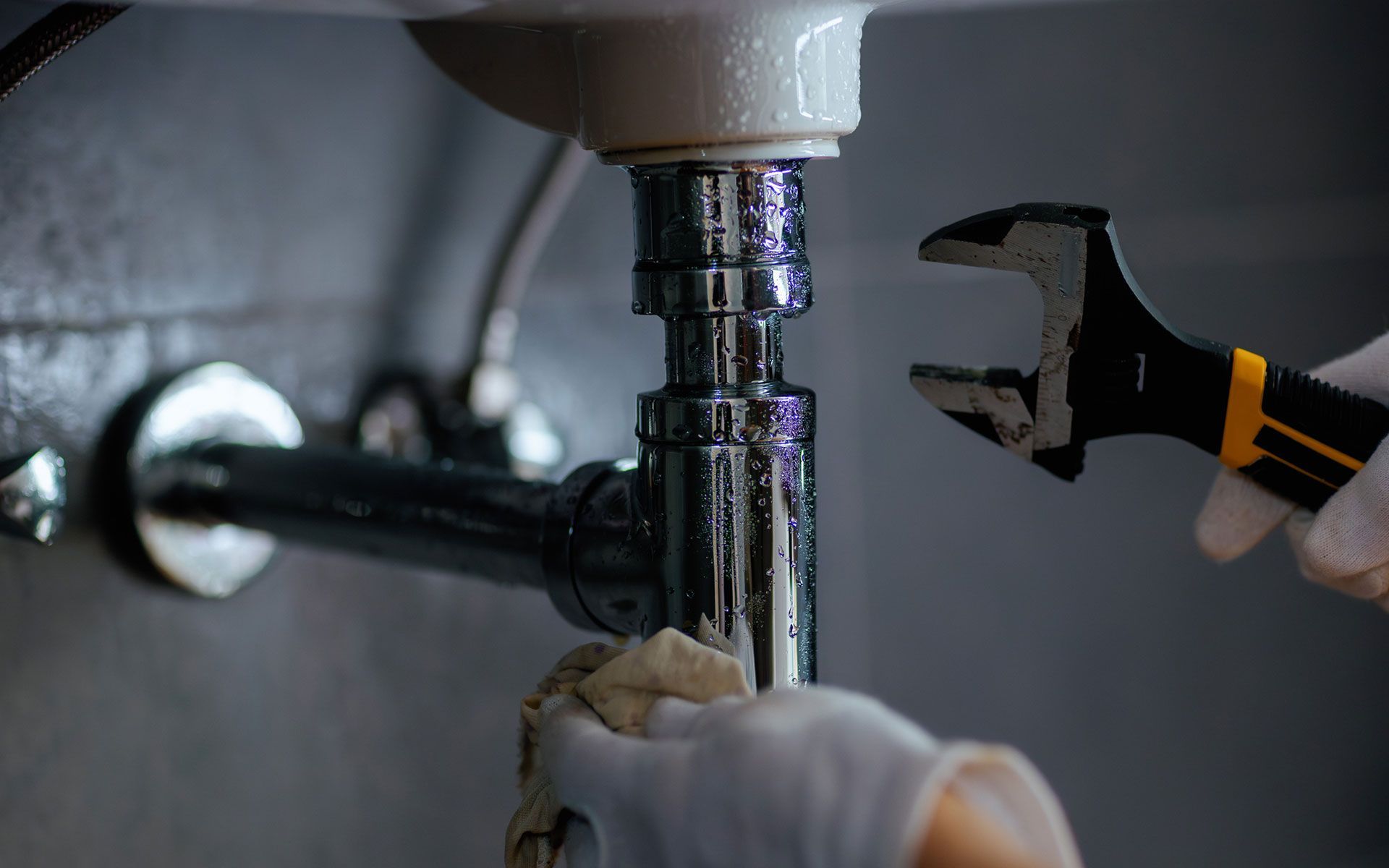 Plumber using a wrench to repair a sink drain, wearing gloves.