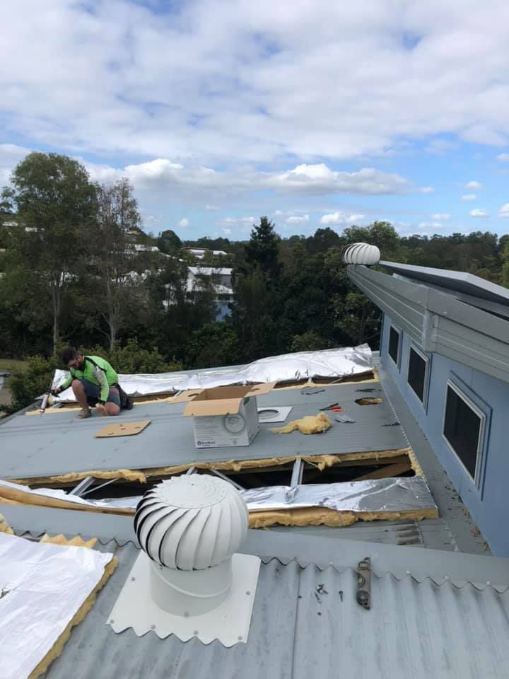A man is working on the roof of a building — Insulation Removal in Arundel QLD
