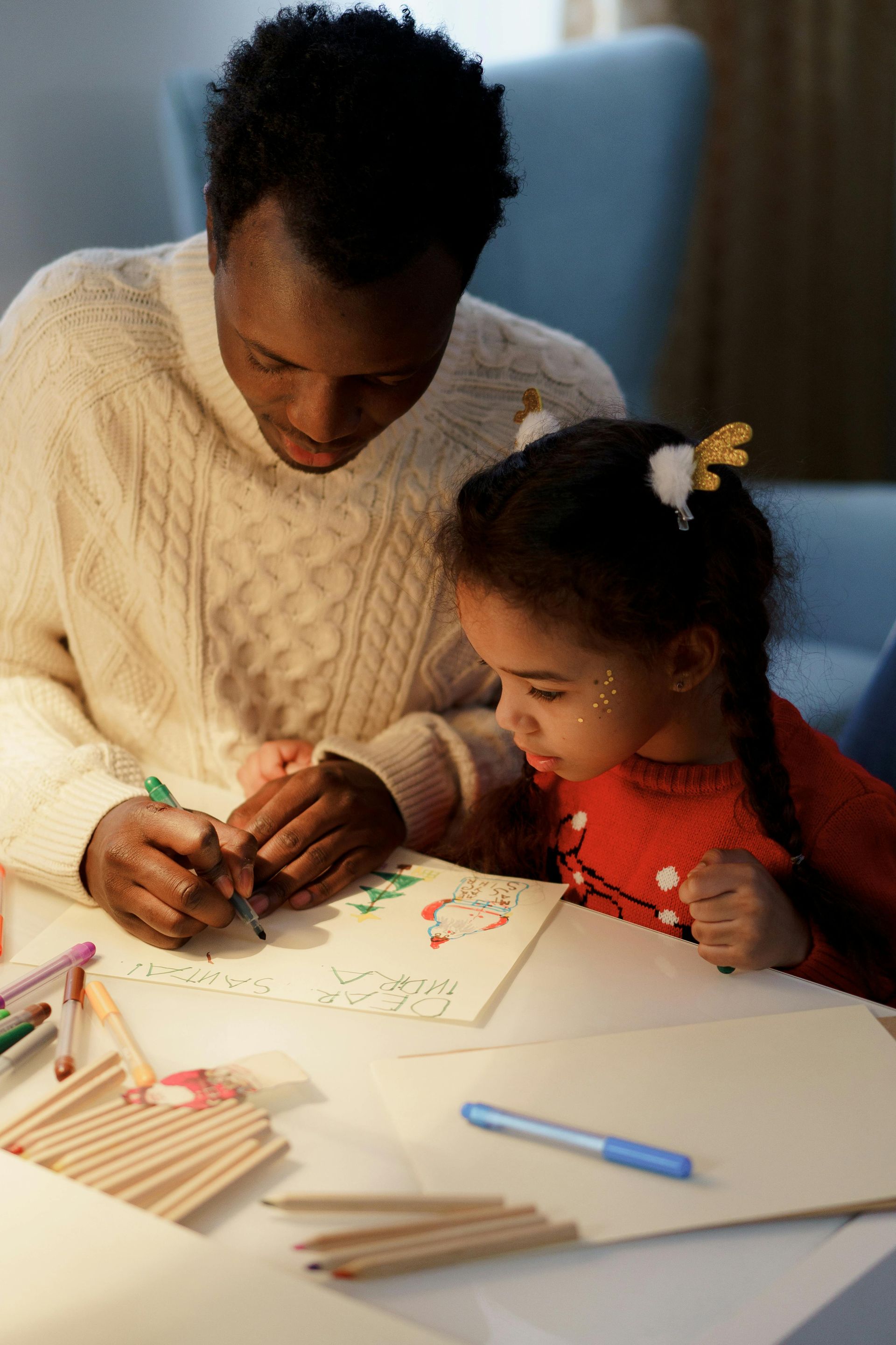 A man and a little girl are sitting at a table drawing with pencils.