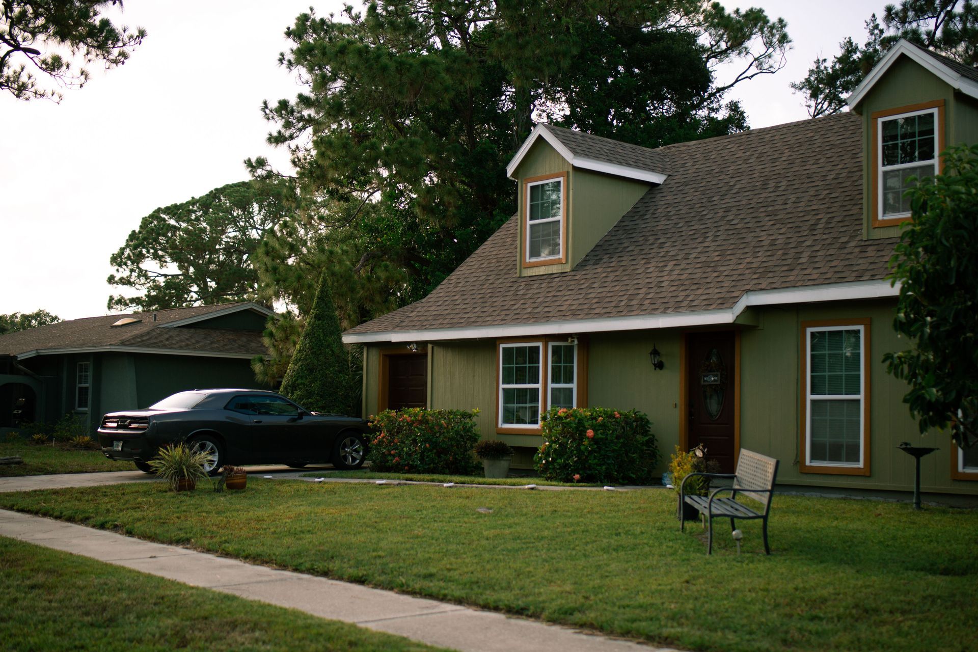 View of green suburban home with a Dodge Challenger parked in the driveway.