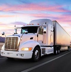 White semi-truck driving on a highway at sunset under a pink-blue sky