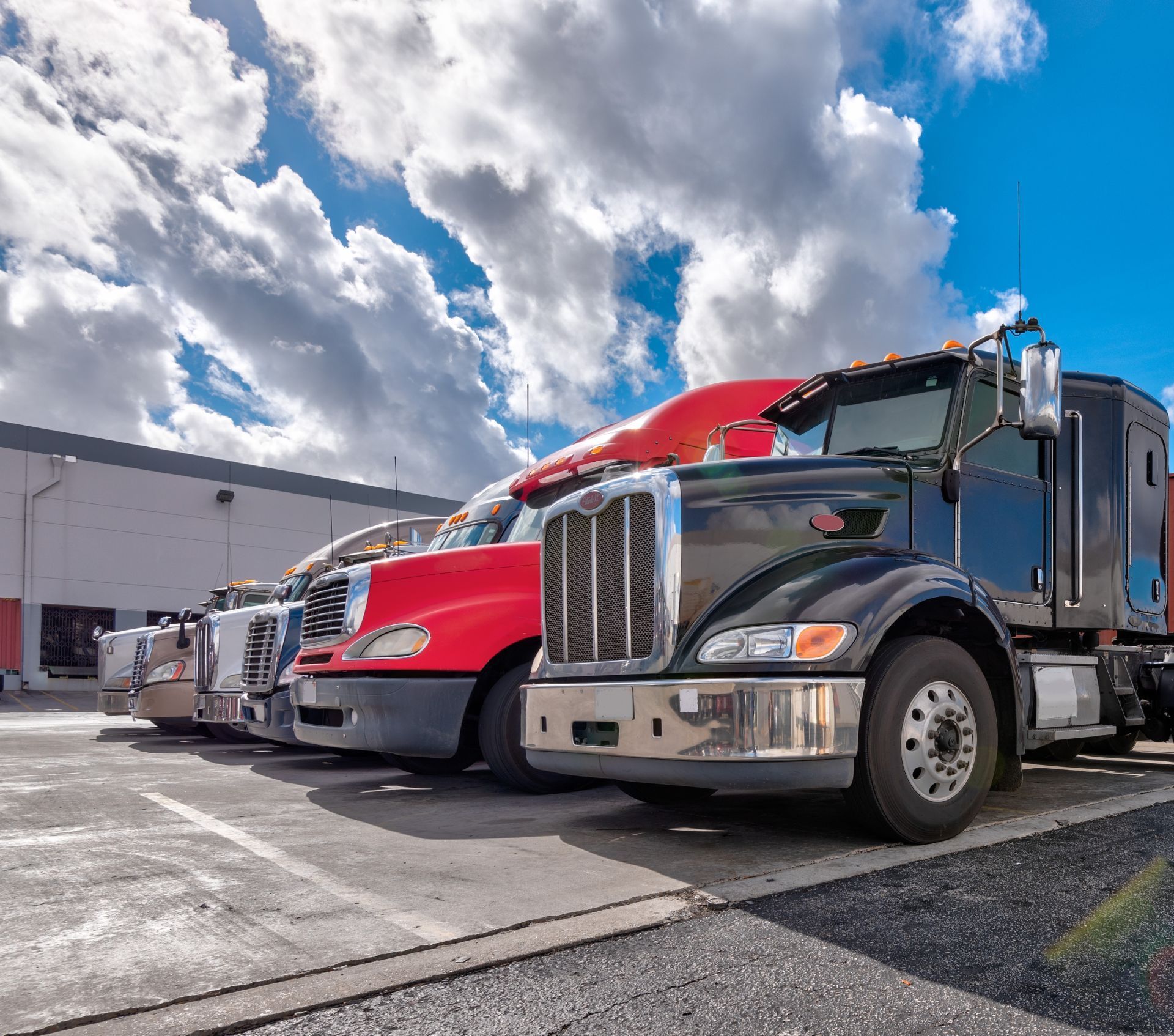 Two parked semi trucks, red and black, in a lot under a cloudy sky