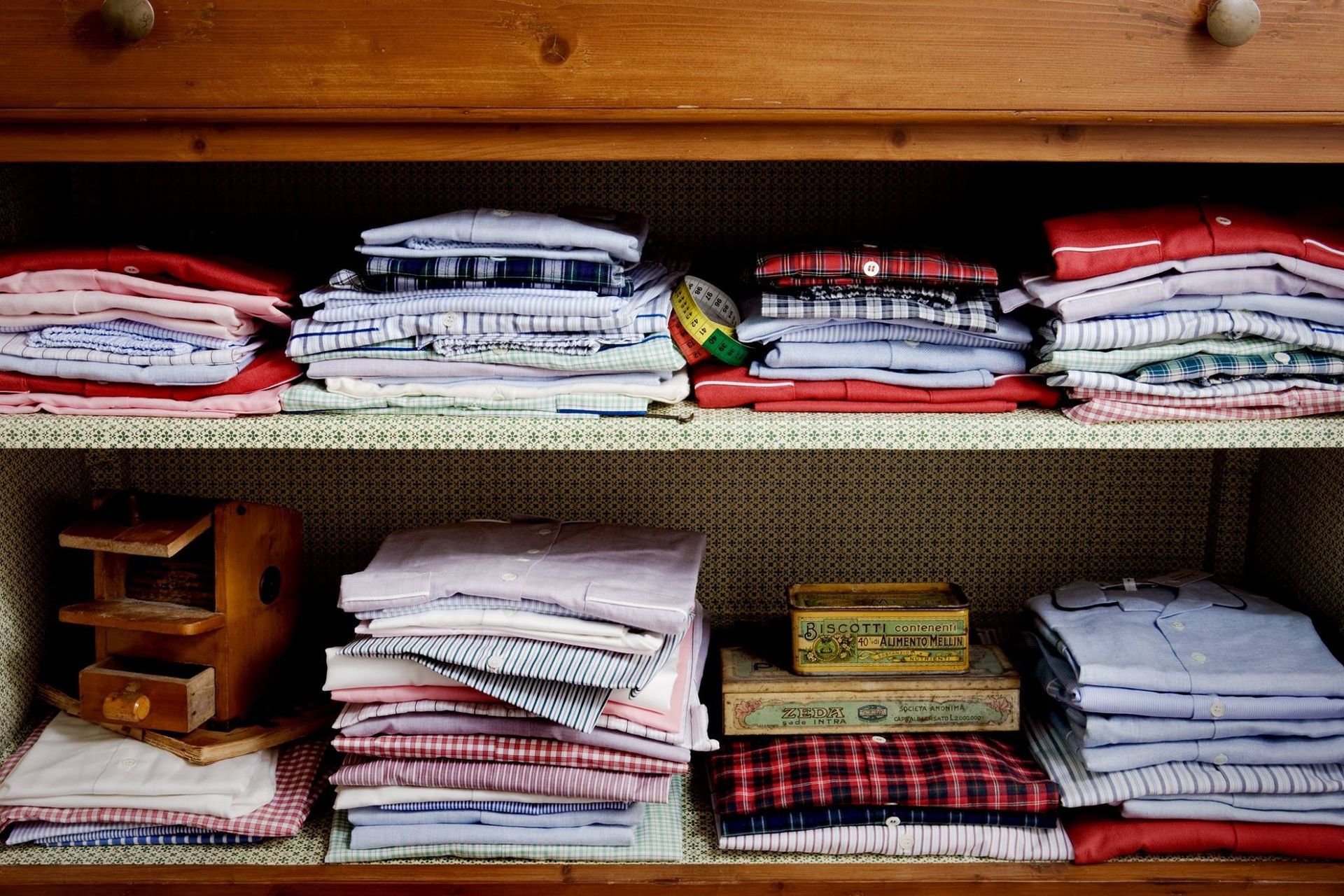 Scaffali di armadietti in legno pieni di camicie ordinatamente piegate di vari colori.