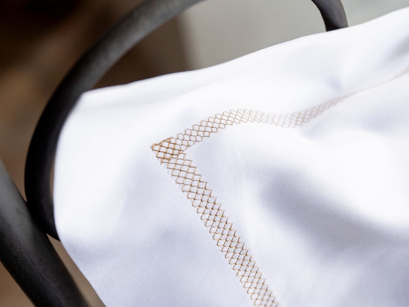 Tovagliolo di lino bianco con bordo cucito marrone, drappeggiato su una sedia scura.