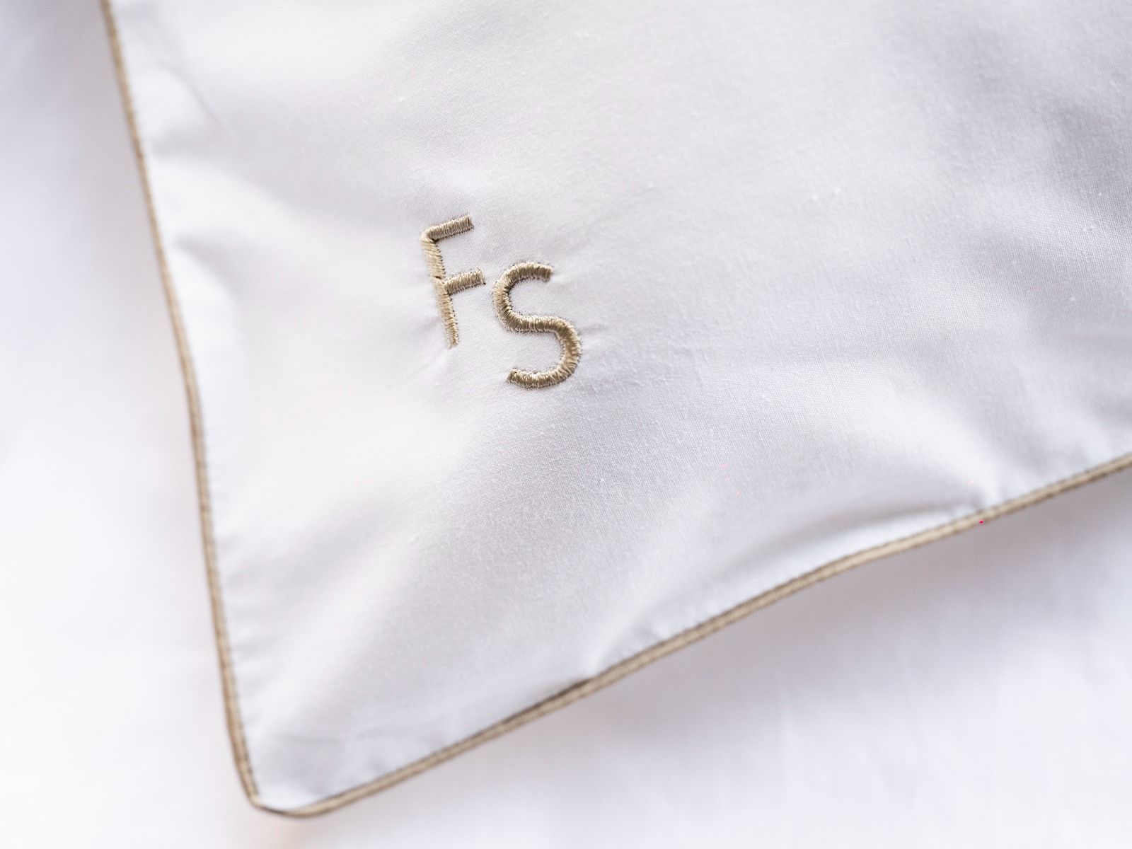Angolo del cuscino bianco con iniziali dorate ricamate 