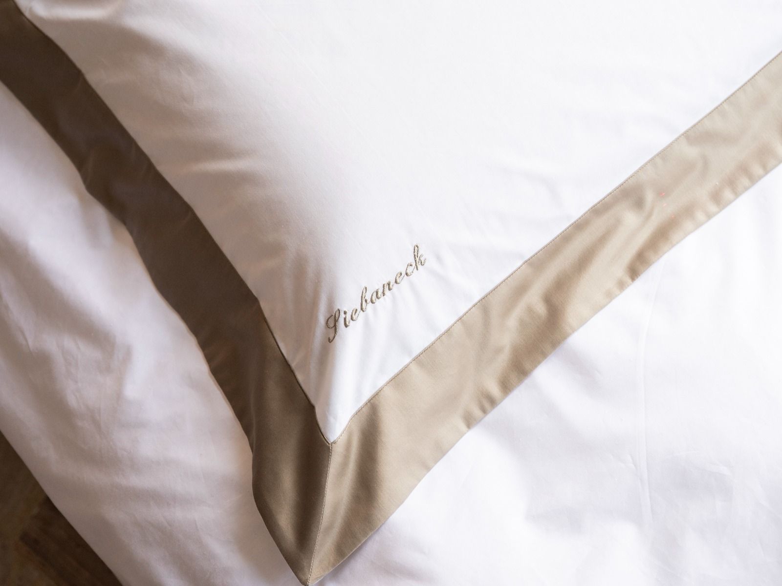 Tovagliolo di lino bianco con bordo cucito marrone, drappeggiato su una sedia scura.