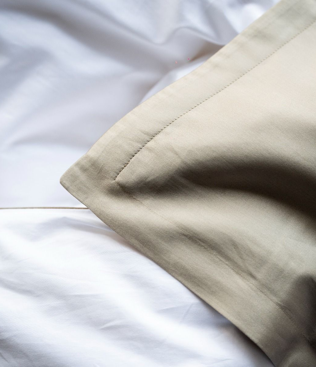 Cuscino beige su lenzuola bianche, angolo in primo piano.