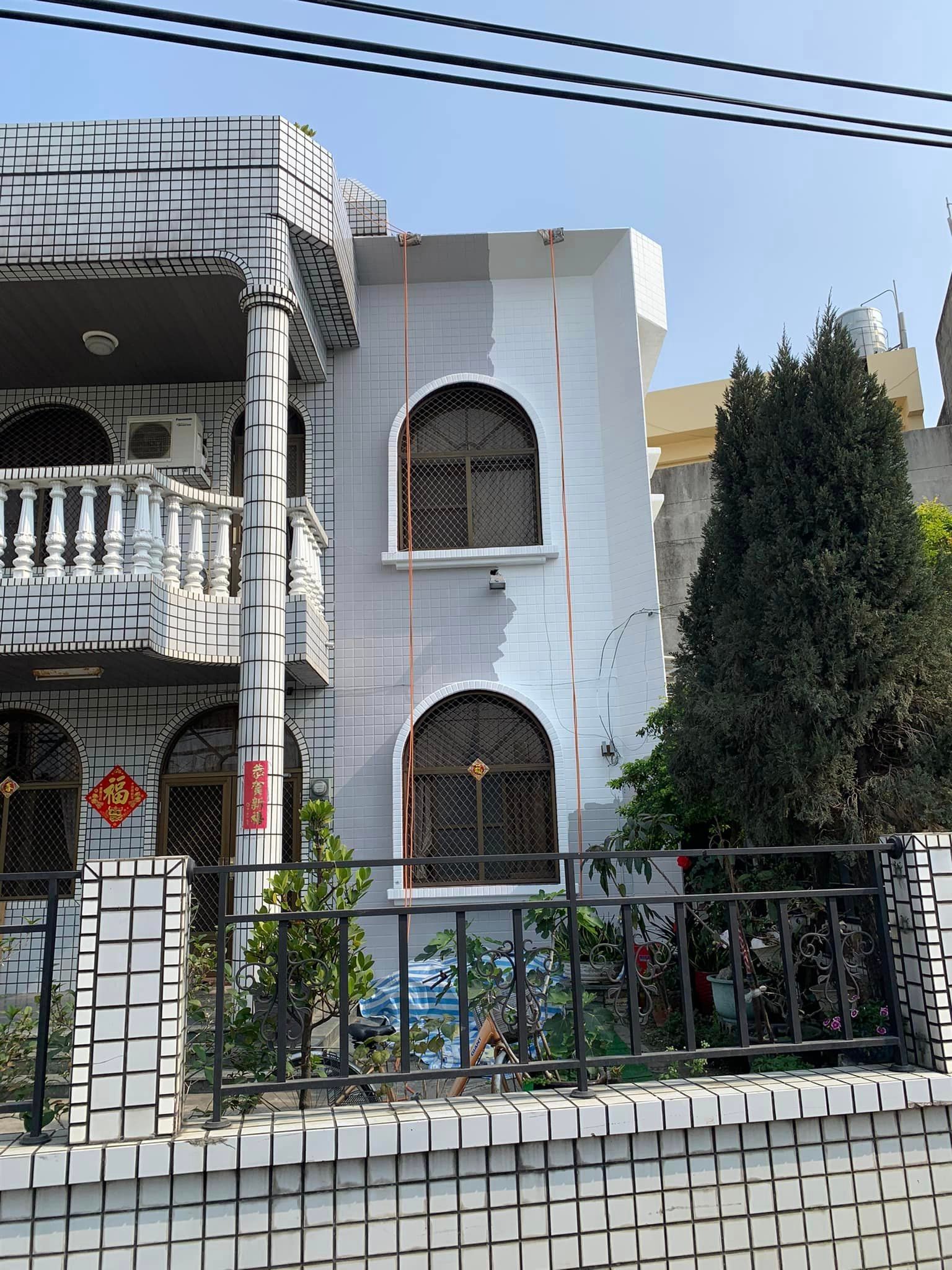 A white house with arched windows is behind a brick fence.