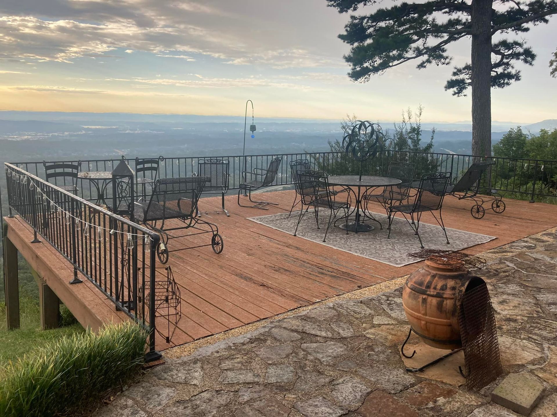 Wooden deck with black wrought-iron tables and chairs overlooking a vast mountain view at sunset.