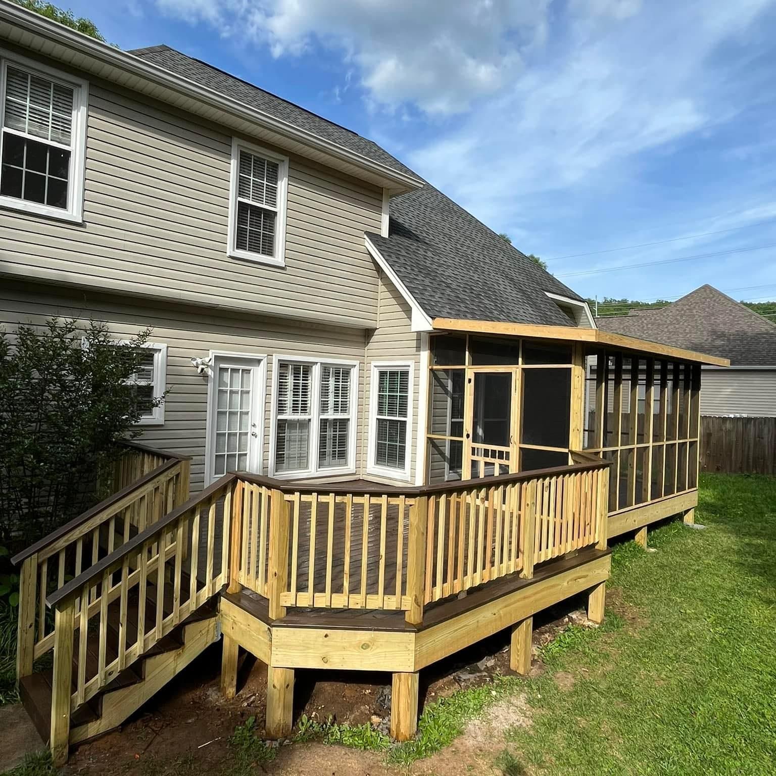 Backyard with wooden deck and screened porch attached to a light-colored house under a blue sky.