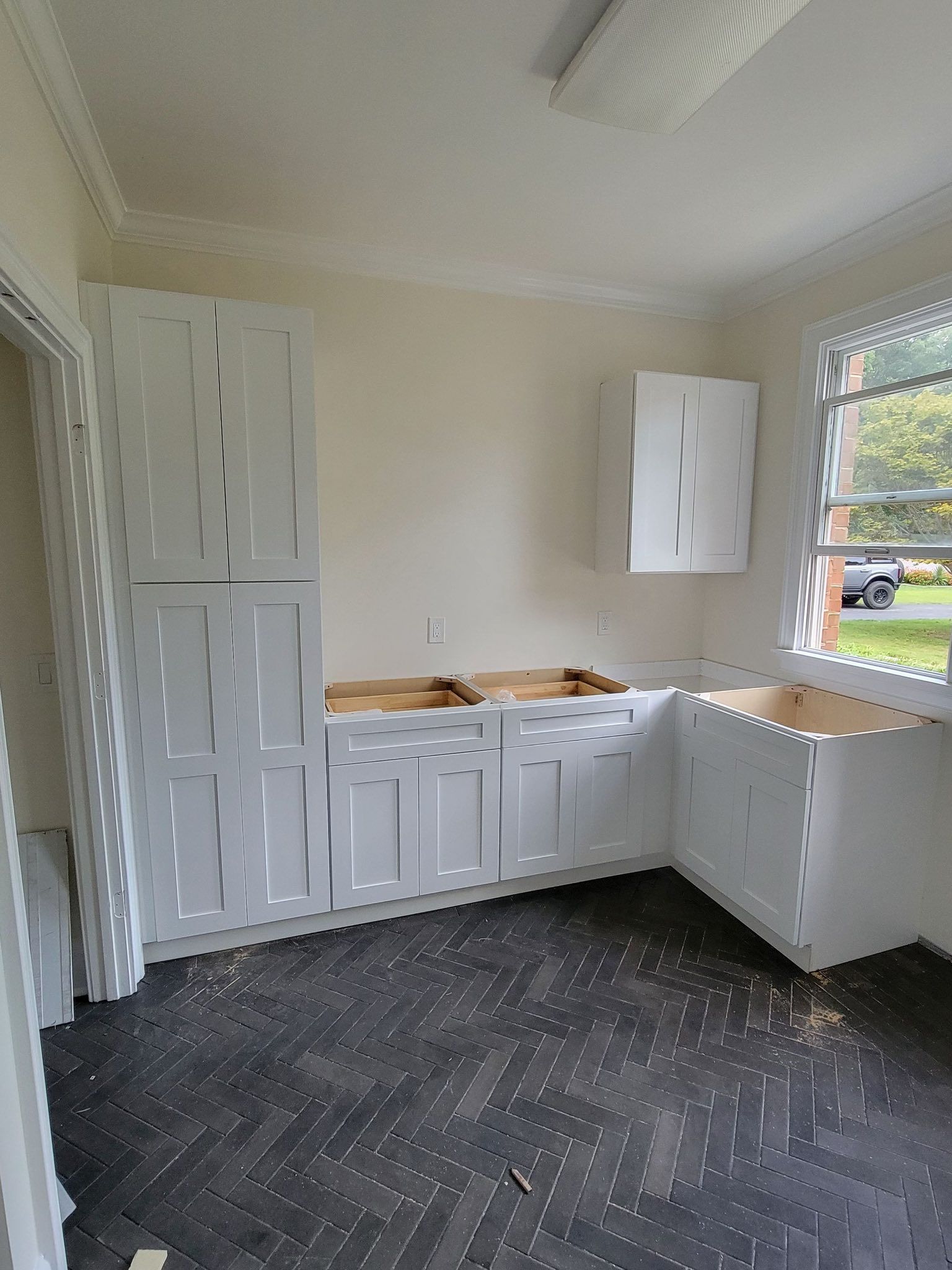 White kitchen cabinets installed in a room with dark flooring and a window.