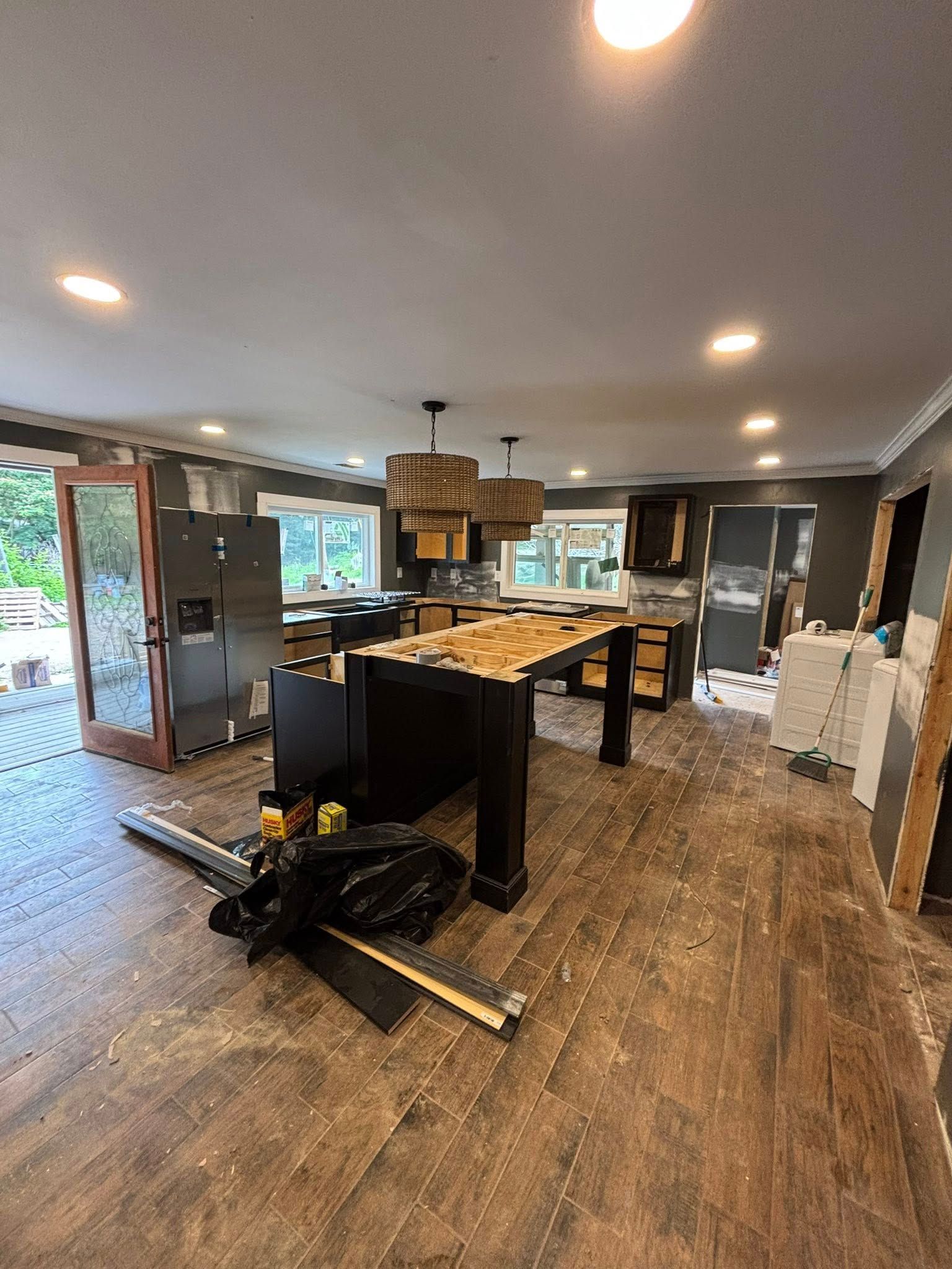 Kitchen under renovation with dark island, cabinets, and debris on wood flooring.