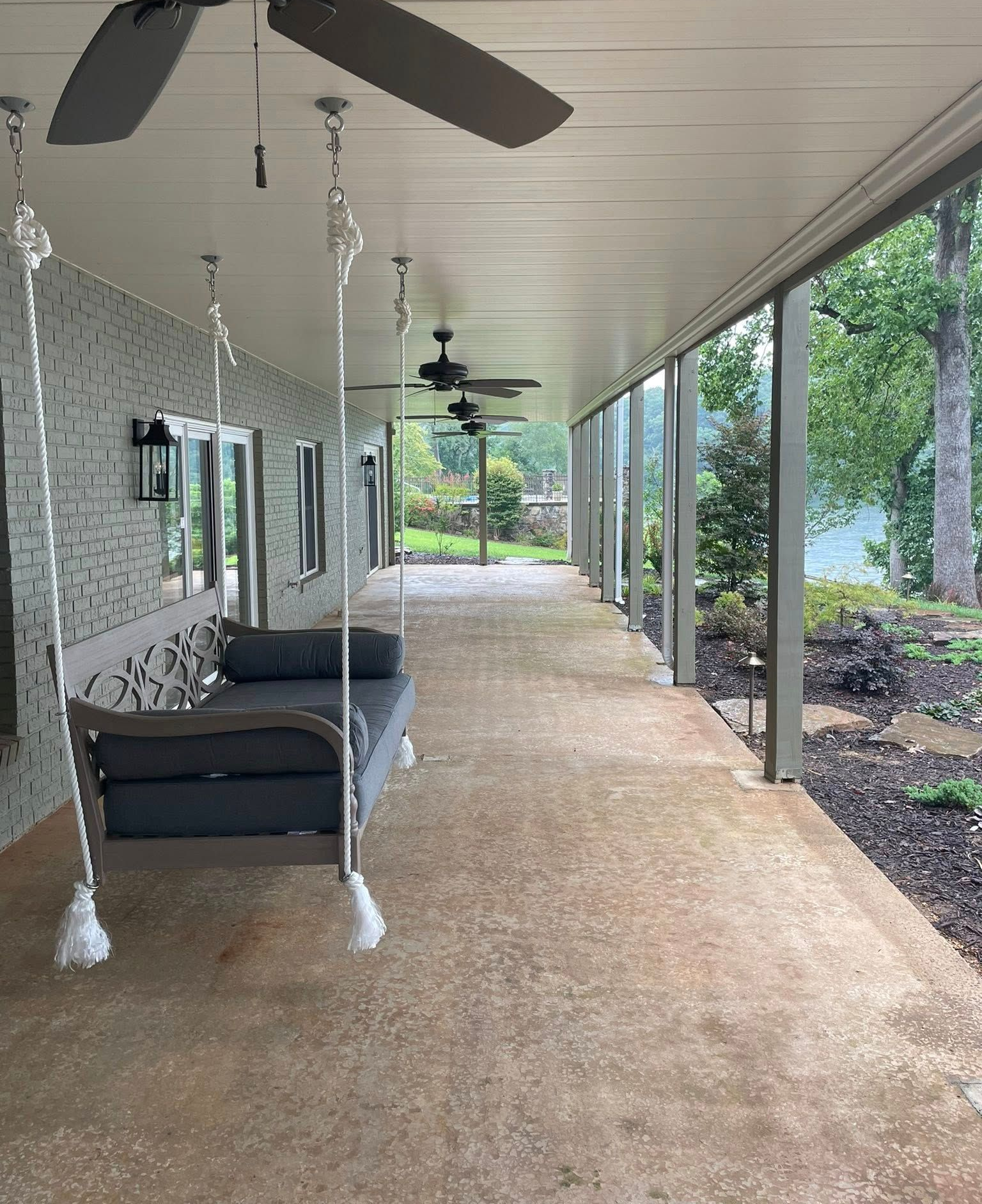 Covered outdoor porch with a swing, brick wall, and ceiling fans overlooking a garden.