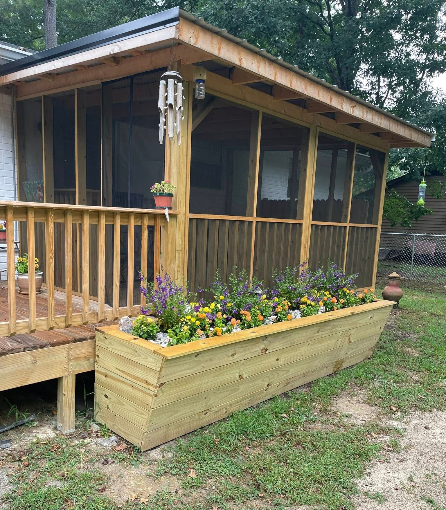 Screened porch with wooden railings, flower box filled with plants, and a small wind chime.