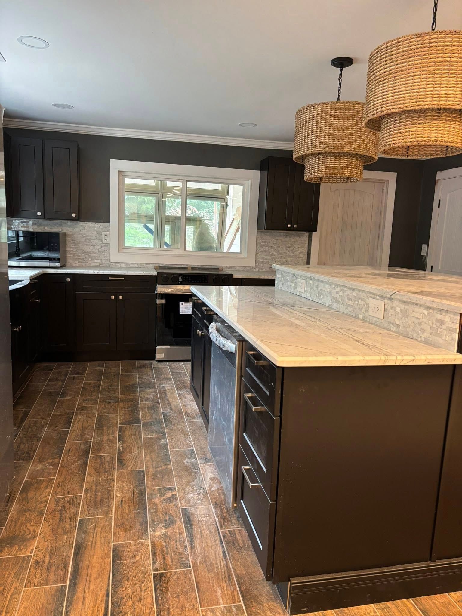 Kitchen with dark cabinets, light countertops, wood-look flooring, and woven pendant lights.