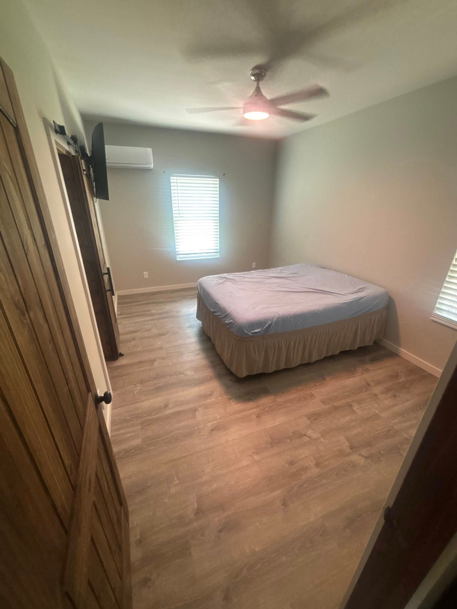 Bedroom with bed, closet, window, and ceiling fan. Light wood-look flooring and neutral walls.