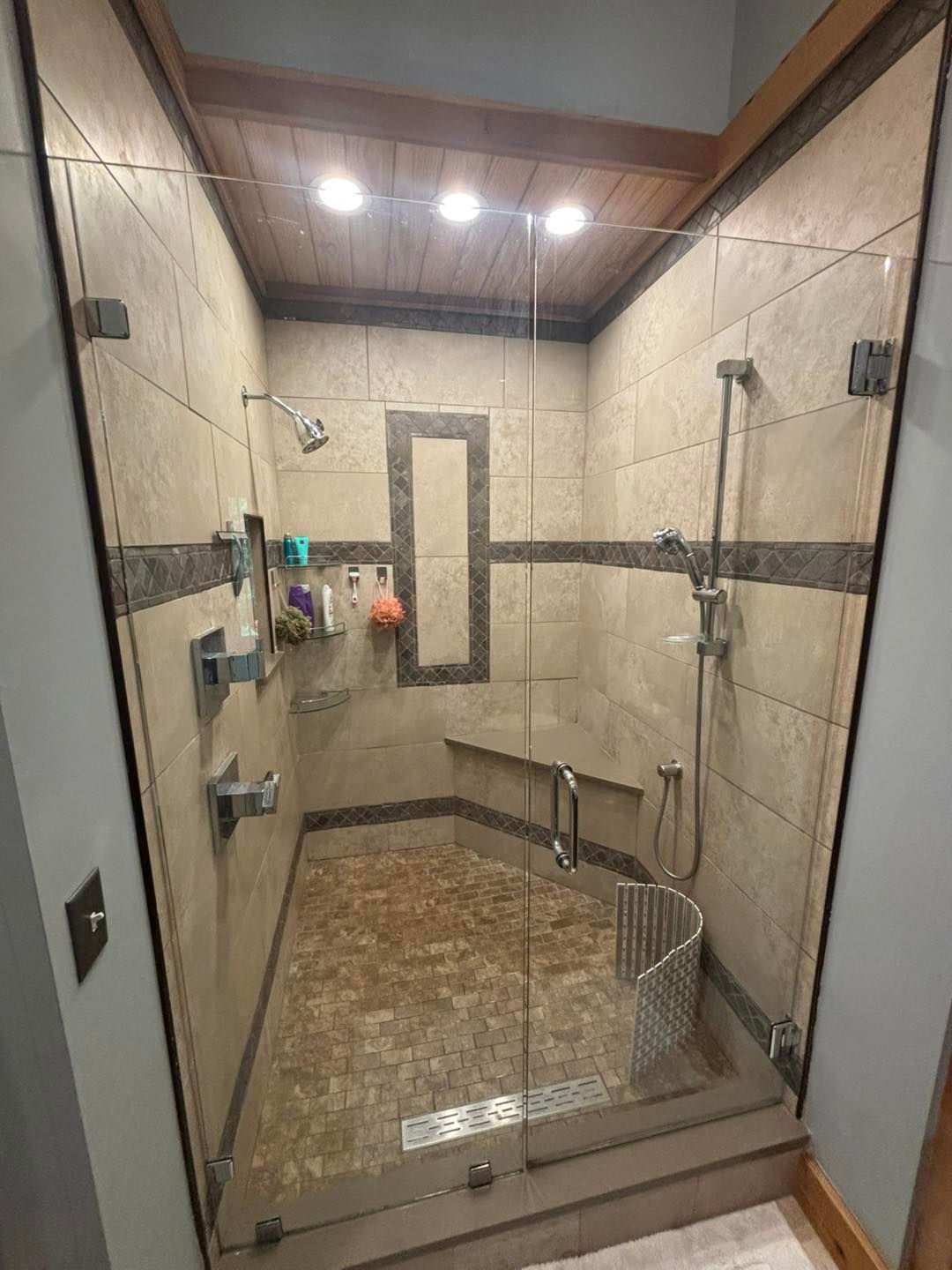 A modern tiled shower with glass doors, a bench, and multiple showerheads; the shower has warm-toned tiles.