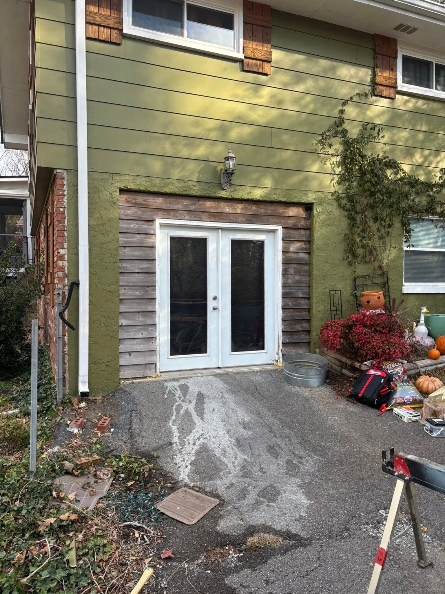 White French doors installed in a house exterior with unfinished wooden siding and a sloped concrete path.