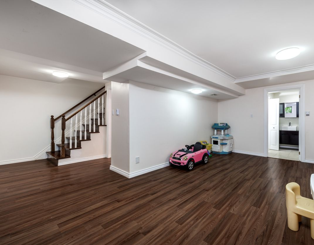 Basement interior with hardwood floors, stairs, toy car, play kitchen, and a bathroom doorway.