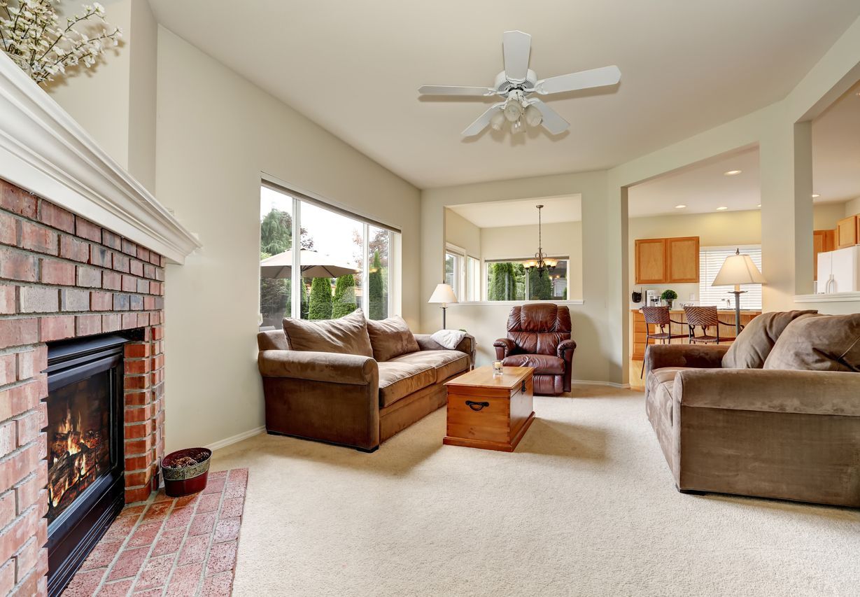 Living room with brick fireplace, brown sofas, window, and view to the kitchen.