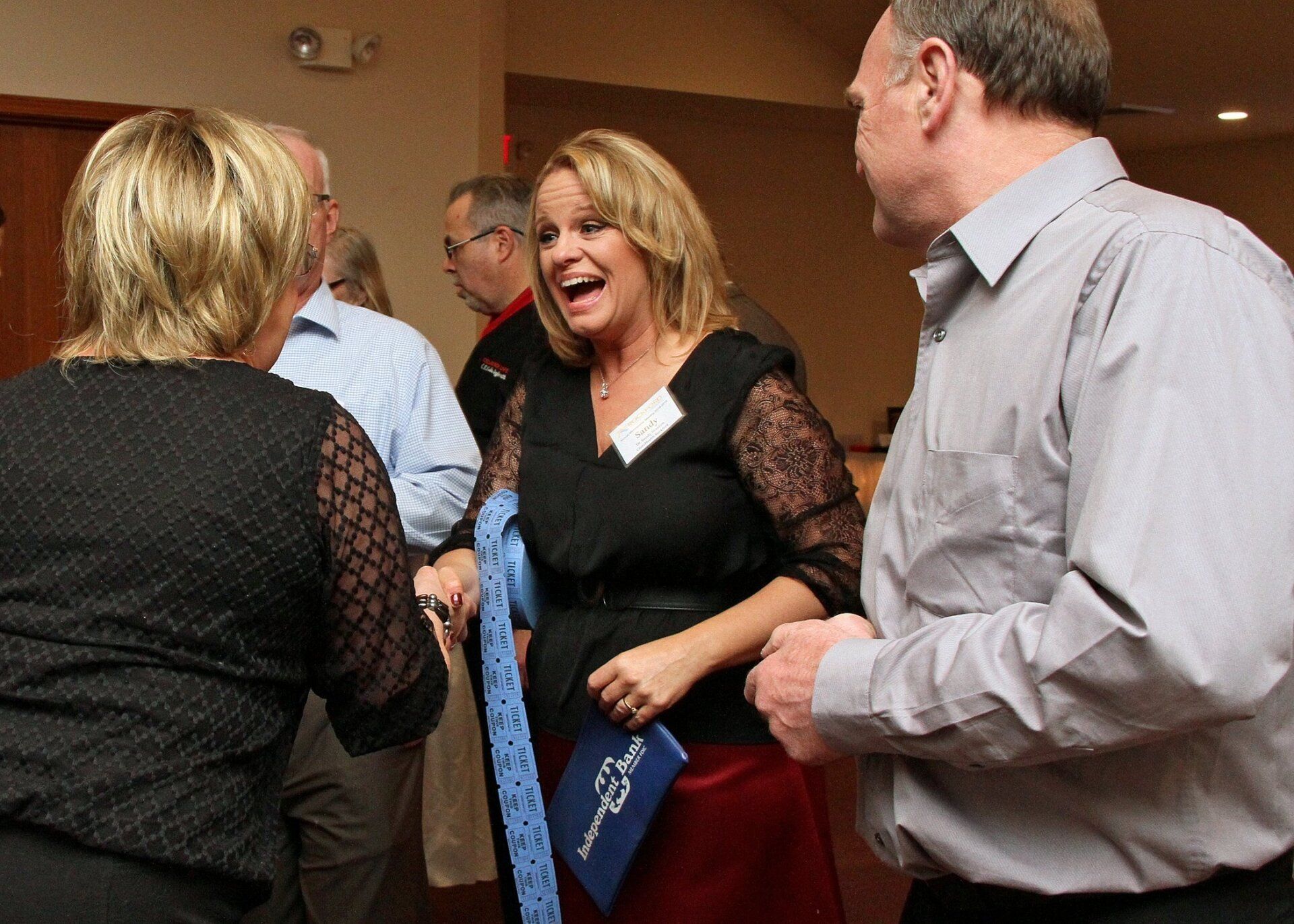 People socializing at a party, woman in black dress laughing, holding a blue tie.