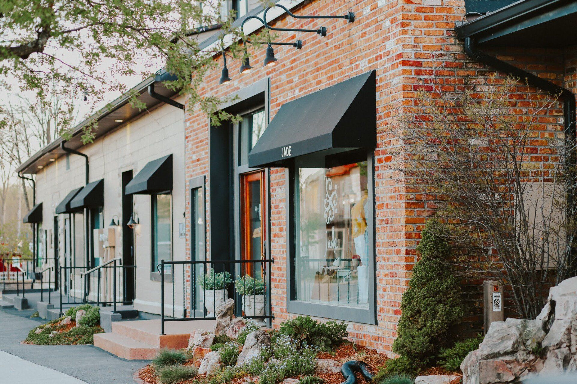 Brick storefront with black awnings and landscaping.