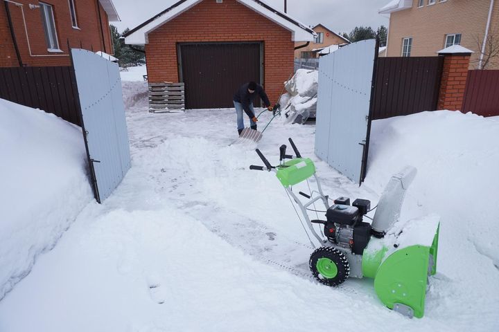 A man is clearing snow from his driveway with a snow blower.