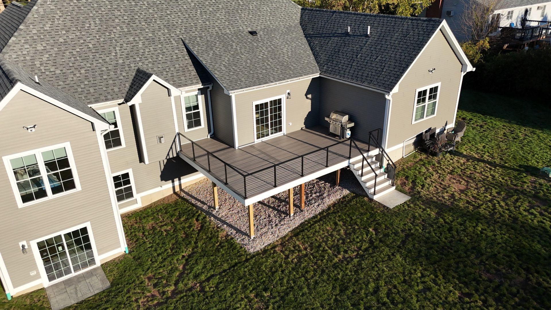 Aerial view of a gray house with a deck. Deck has dark railings and overlooks a grassy yard.