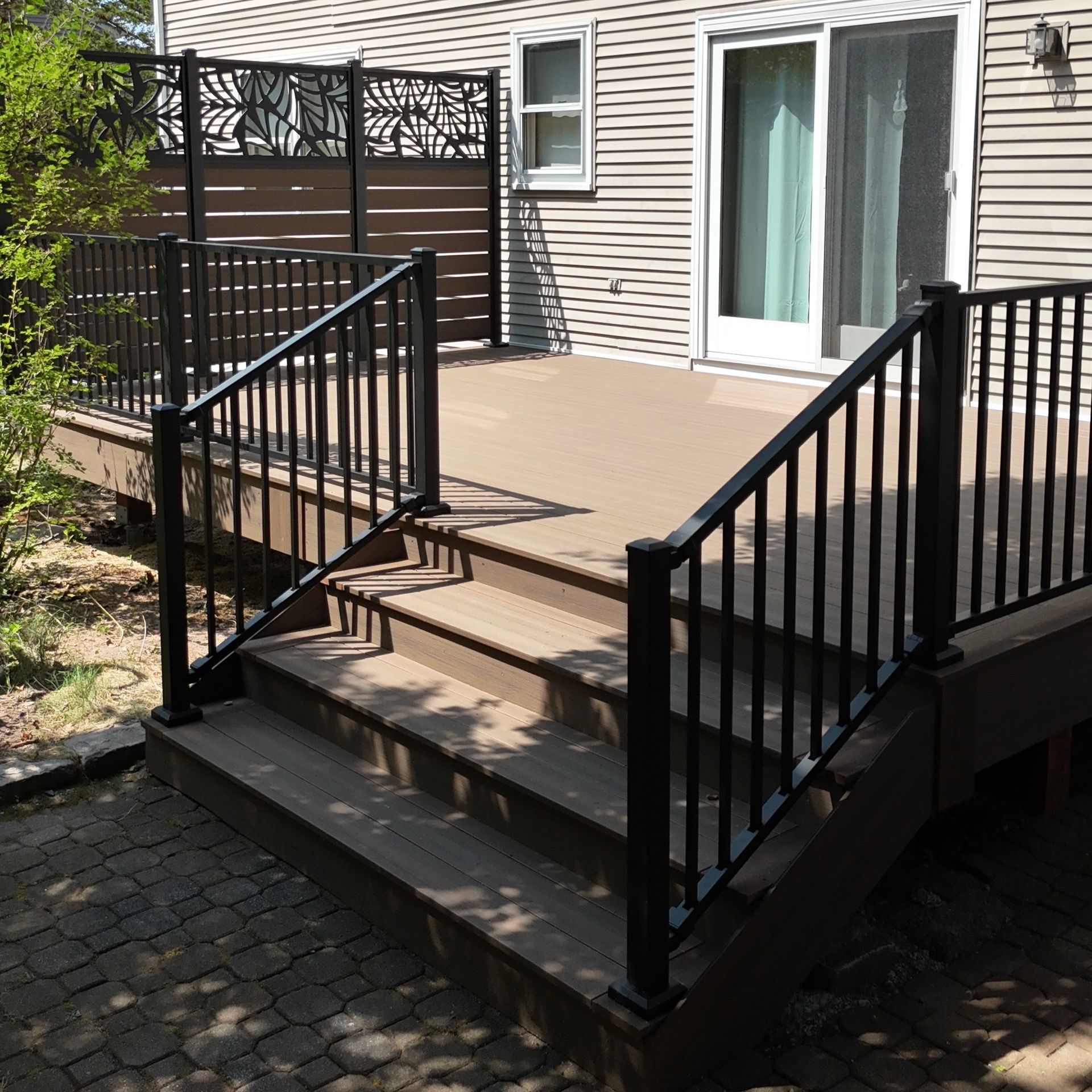 Wooden deck with black railings and steps leading down to a brick patio.