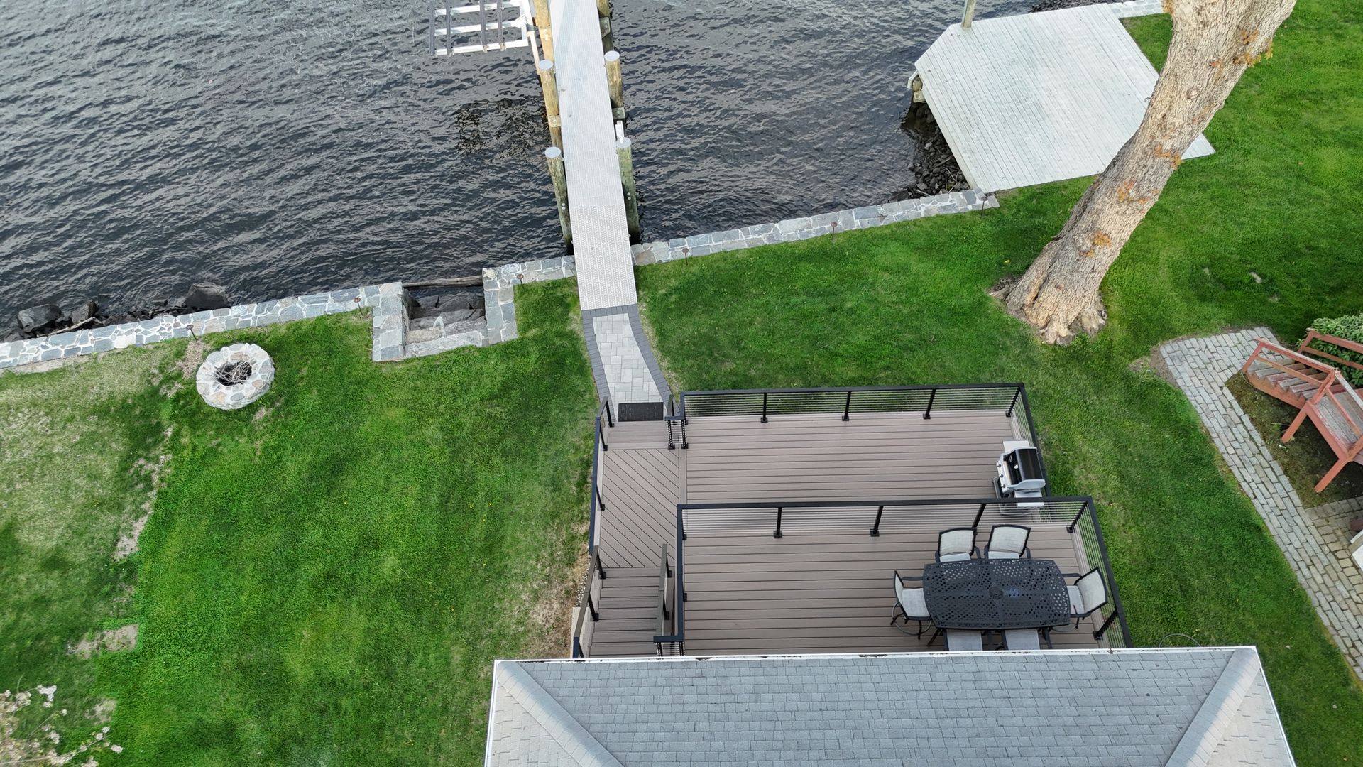 Overhead view of a house and dock on a lake with green grass and a gray deck and roof.