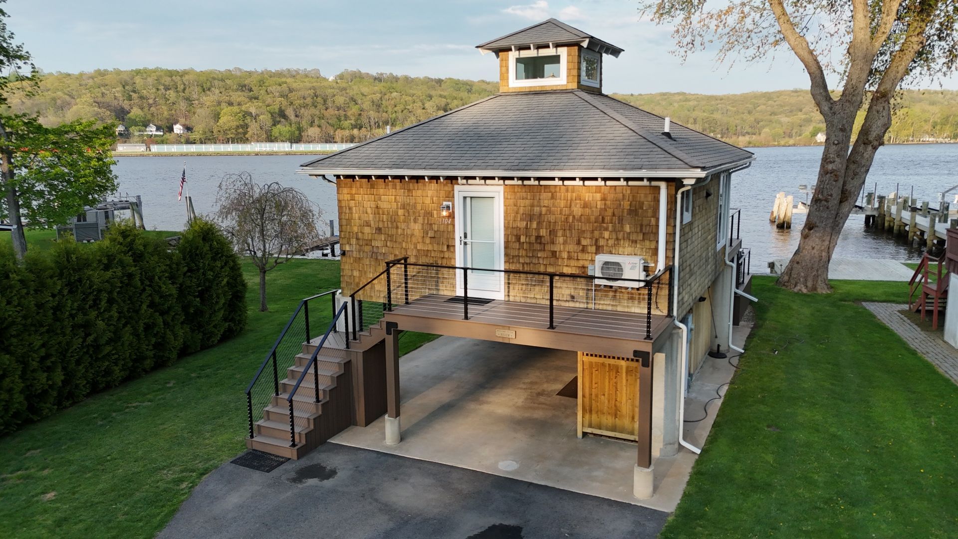Small house on stilts with a deck, driveway, and stairs by a lake.