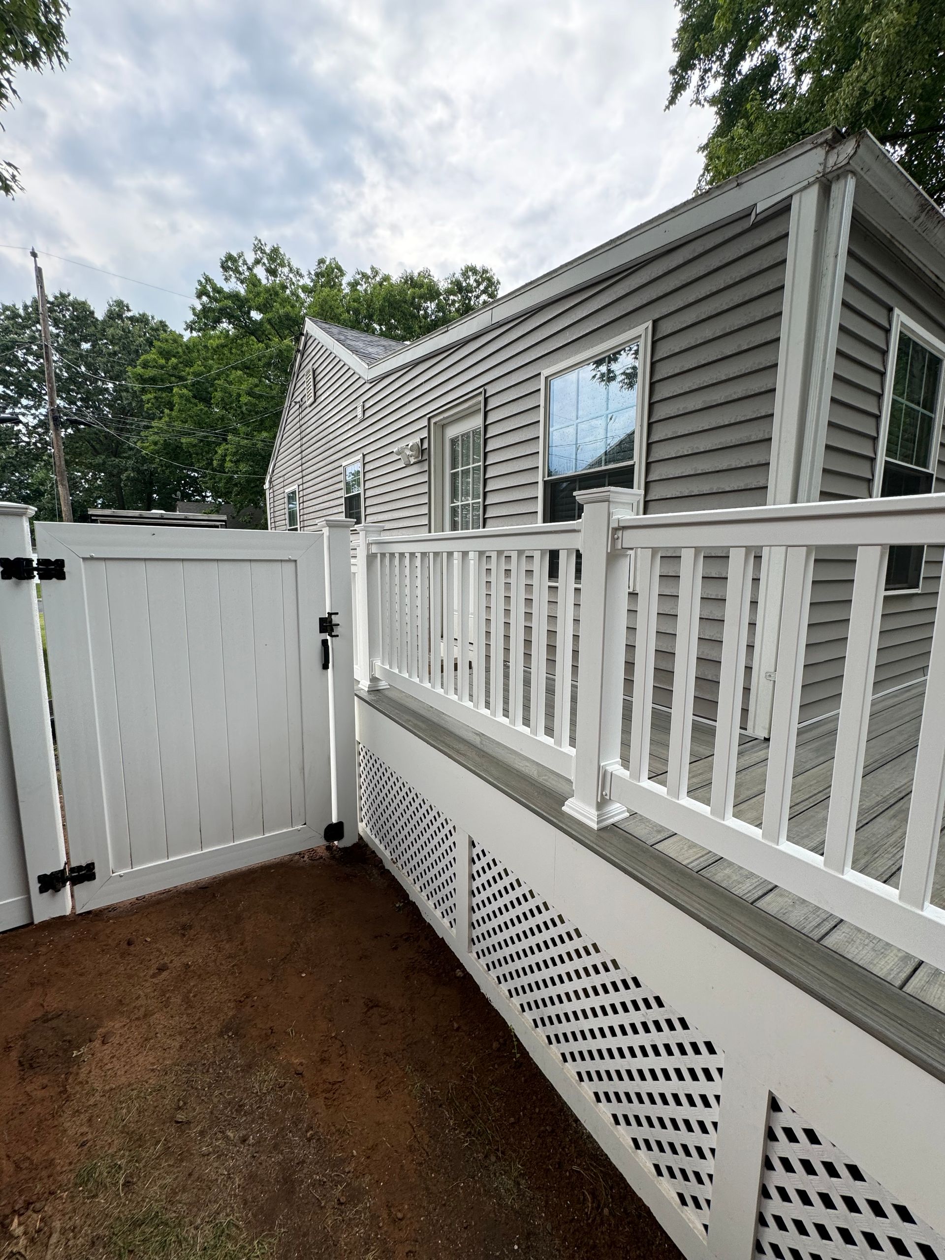 White fence and deck with gray siding house in background.