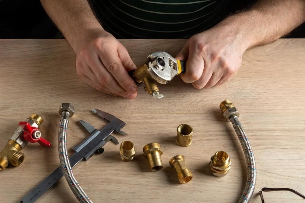 A man is fixing a faucet with a wrench on a wooden table.