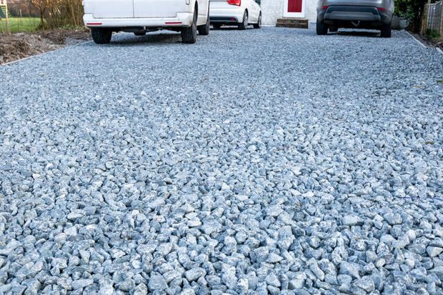 A gravel driveway leading up to a house with three parked cars.