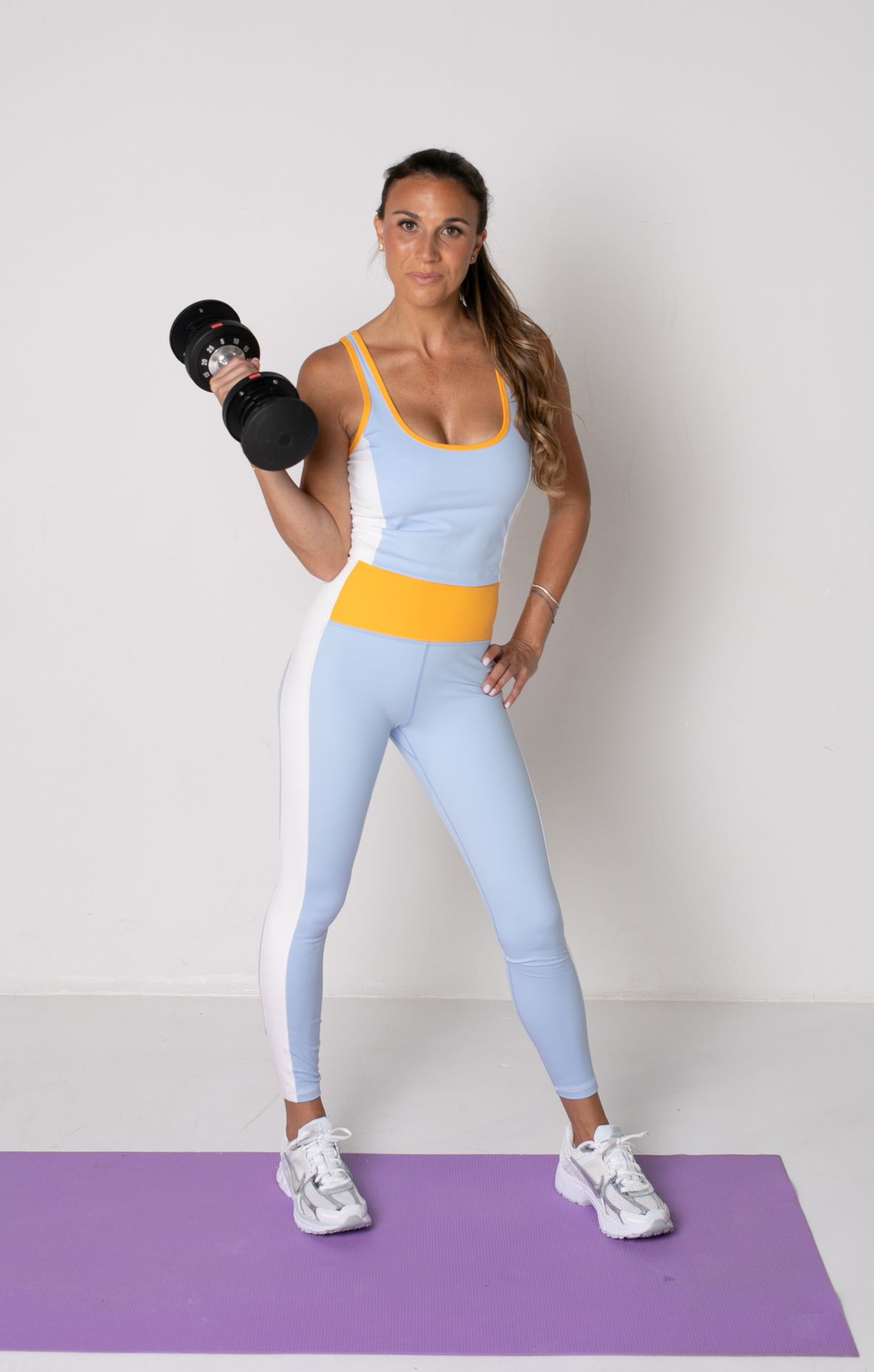 A woman is standing on a yoga mat holding a dumbbell.
