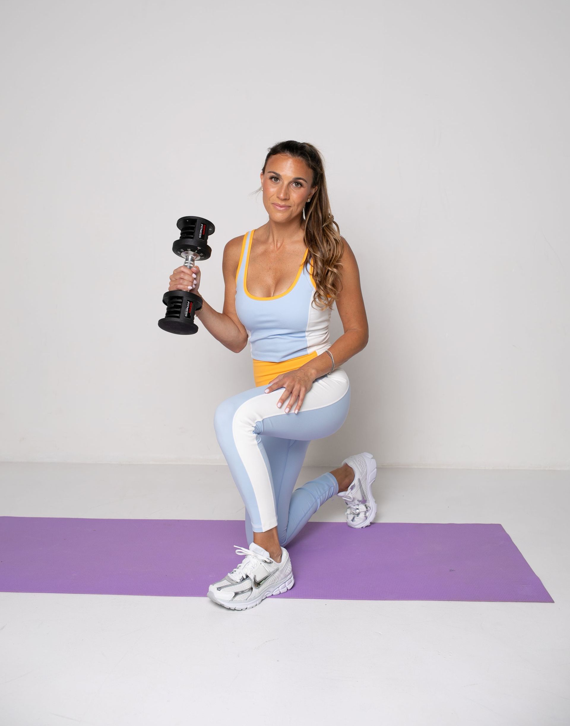 A woman is squatting on a yoga mat while holding a dumbbell.