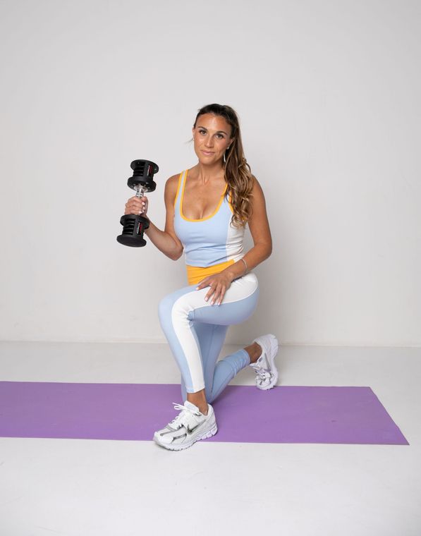 A woman is squatting on a yoga mat while holding a dumbbell.