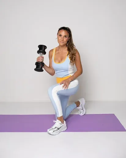 A woman is squatting on a yoga mat while holding a dumbbell.
