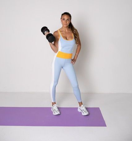 A woman is standing on a yoga mat holding a dumbbell.