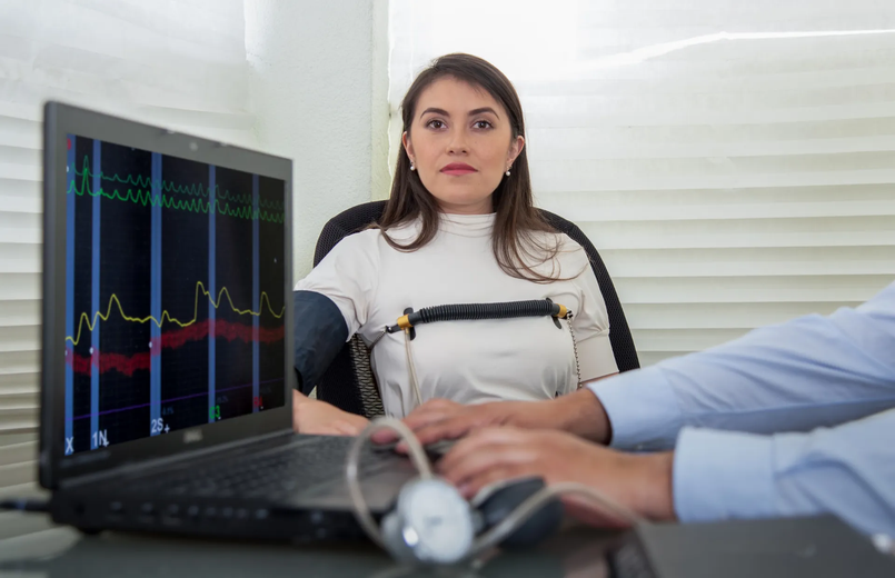 Woman undergoing a polygraph test, connected to sensors, with graphs displayed on laptop screen.