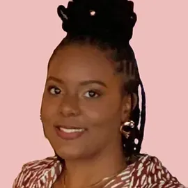 A woman with dreadlocks is smiling and wearing a zebra print shirt.